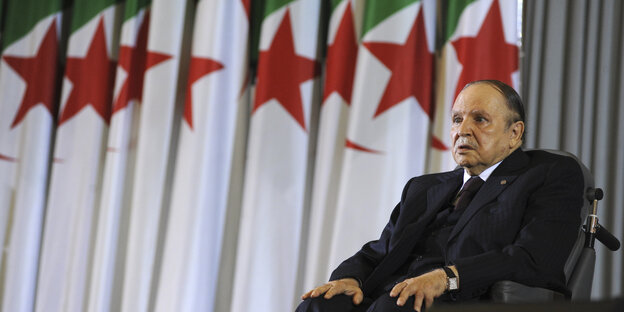 Präsident Abdelaziz Bouteflika sitzt auf einem Rollstuhl. Im Hintergrund sind algerische Fahnen. Präsident Abdelaziz Bouteflika sitzt auf einem Rollstuhl. Im Hintergrund sind algerische Fahnen.