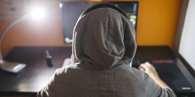 Ein Mensch mit Kapuze vor einem Computer Ein Mensch mit Kapuze vor einem Computer
