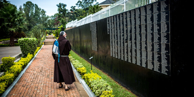 Ein Moench spaziert entlang der Wand des Genozid-Memorials in Ruanda Ein Moench spaziert entlang der Wand des Genozid-Memorials in Ruanda