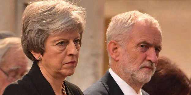 Theresa May sitzt neben Jeremy Corbyn, beide schauen skeptisch Theresa May sitzt neben Jeremy Corbyn, beide schauen skeptisch