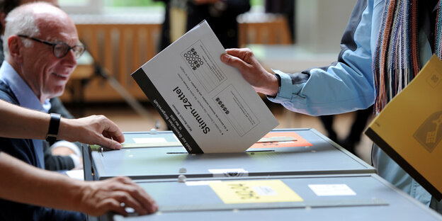 Eine Person steckt einen Wahlzettel in eine Wahlbox. Eine Person steckt einen Wahlzettel in eine Wahlbox.