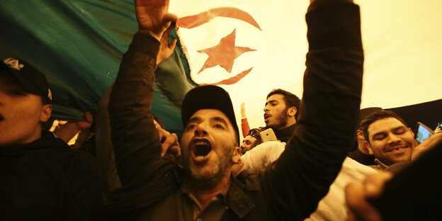 Ein Mann unter einer algerischen Flagge hebt die Arme. Ein Mann unter einer algerischen Flagge hebt die Arme.
