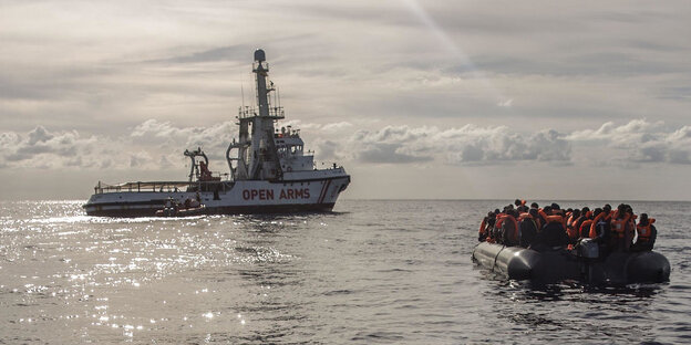 Menschen in einem Schlauchboot vor einem Schiff mit der Aufschrift "Open Arms"