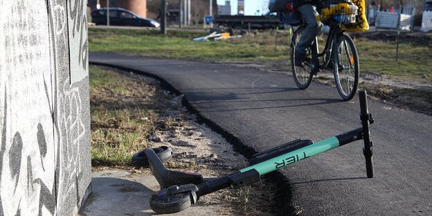 Die Lenkstange eines elektrischen Tretrollers liegt auf einem Radwege. Ein Radfahrer fährt daran vorbei Die Lenkstange eines elektrischen Tretrollers liegt auf einem Radwege. Ein Radfahrer fährt daran vorbei