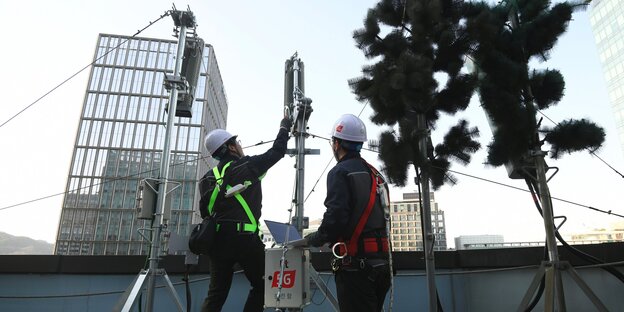 Arbeiter montieren getarnte 5G-Antennten auf einem Hausdach in Seoul. Arbeiter montieren getarnte 5G-Antennten auf einem Hausdach in Seoul.