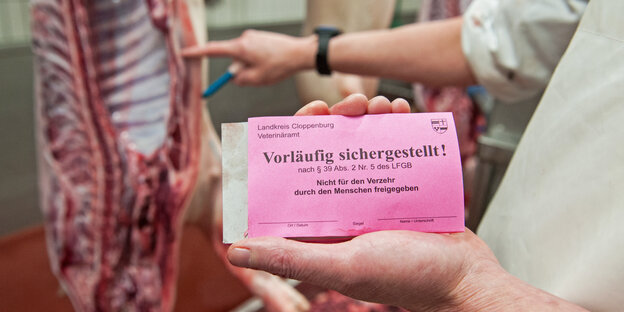 Vor einer Schweinehälfte zeigt ein Schlachter ein Schild mit der Aufschrift "vorläufig sichergestellt" Vor einer Schweinehälfte zeigt ein Schlachter ein Schild mit der Aufschrift "vorläufig sichergestellt"