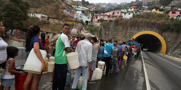 Menschen stehen mit leeren Kanistern in einer langen Schlange vor einer Wasserausgabestelle in Caracas, Venezuela Menschen stehen mit leeren Kanistern in einer langen Schlange vor einer Wasserausgabestelle in Caracas, Venezuela