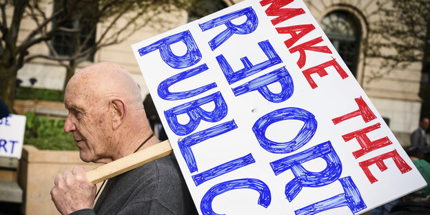 Mann mit Schild, darauf steht in rot und blau: "Make the Report public" Mann mit Schild, darauf steht in rot und blau: "Make the Report public"