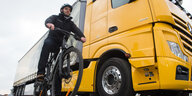 ein Radfahrer mit Helm wartet neben einem riesigen gelben Lkw