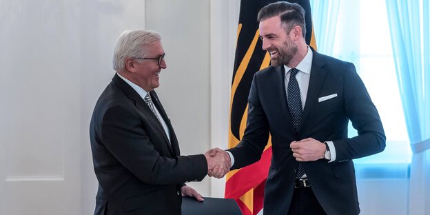 Christoph Metzelder und Frank-Walter Steinmeier schütteln sich die Hand vor einer Deutschlandfahne