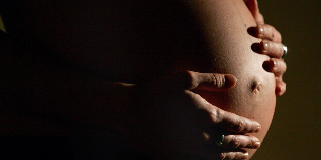 Der Bauch einer schwangeren Frau und ihre darauf liegenden Hände Der Bauch einer schwangeren Frau und ihre darauf liegenden Hände