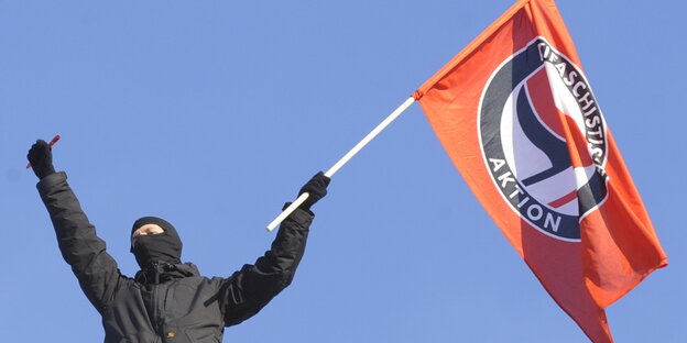 Schwarz gekleideter Antifaschist mit Antifa-Fahne in der Hand Schwarz gekleideter Antifaschist mit Antifa-Fahne in der Hand