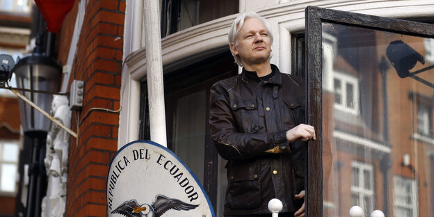 Julian Assange in Lederjacke aus einer Balkontür schauend Julian Assange in Lederjacke aus einer Balkontür schauend