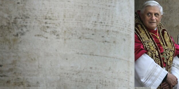 Joseph Ratzinger als Papst steht neben einer Säule und schaut belustigt Joseph Ratzinger als Papst steht neben einer Säule und schaut belustigt