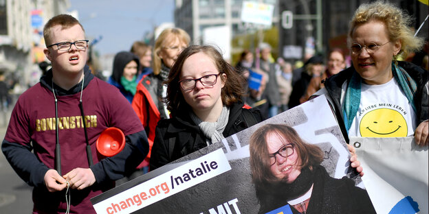 Drei Personen tragen ein Plakat auf einer Demonstration Drei Personen tragen ein Plakat auf einer Demonstration