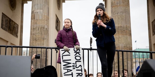 Zwei junge Frauen stehen vor dem Brandenburger Tor, eine spricht in ein Mikrofon Zwei junge Frauen stehen vor dem Brandenburger Tor, eine spricht in ein Mikrofon
