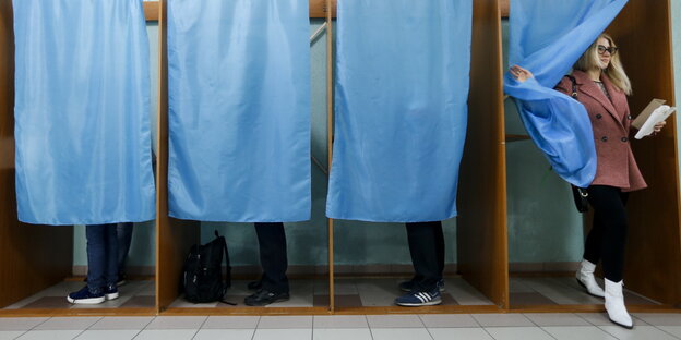 vier besetzte Wahlkabinen, aus einer kommt eine Frau heraus vier besetzte Wahlkabinen, aus einer kommt eine Frau heraus