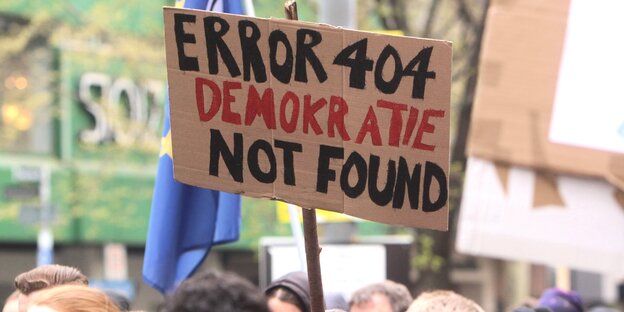 Bei einer Demo wird ein Schild mit der Aufschrift: „Error 404 Demokratie not found“ hochgehalten Bei einer Demo wird ein Schild mit der Aufschrift: „Error 404 Demokratie not found“ hochgehalten
