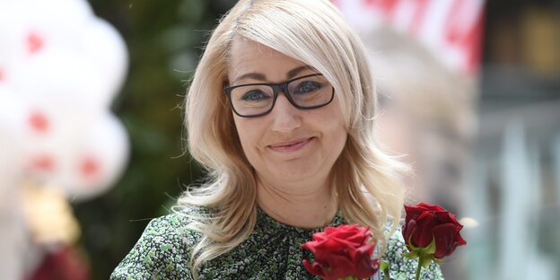 Eine Frau mit roten Rosen in der Hand lächelt in die Kamera. Eine Frau mit roten Rosen in der Hand lächelt in die Kamera.