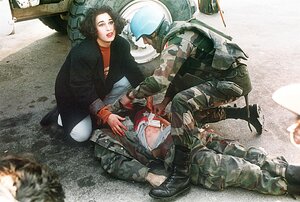 Ein Mann in Militärkleidung liegt am Boden, er ist verletzt, eine Frau und ein Mann knien neben ihm Ein Mann in Militärkleidung liegt am Boden, er ist verletzt, eine Frau und ein Mann knien neben ihm