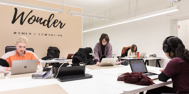 Frauen in einem Büro vor ihren aufgeklappten Macbooks. An der Wand steht Wonder Womens Coworking. Frauen in einem Büro vor ihren aufgeklappten Macbooks. An der Wand steht Wonder Womens Coworking.