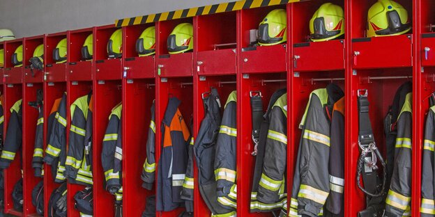 Feuerwehrkleidung (Helme, Jacken und Hosen) in einem roten Schrank Feuerwehrkleidung (Helme, Jacken und Hosen) in einem roten Schrank