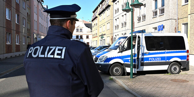Polizist steht vor Polizeiauto bei Razzia in Cottbus Polizist steht vor Polizeiauto bei Razzia in Cottbus