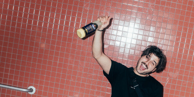 Ein junger Mann mit Schnurrbart und irrem Blick hält eine Flasche Eierlikör in der Hand Ein junger Mann mit Schnurrbart und irrem Blick hält eine Flasche Eierlikör in der Hand