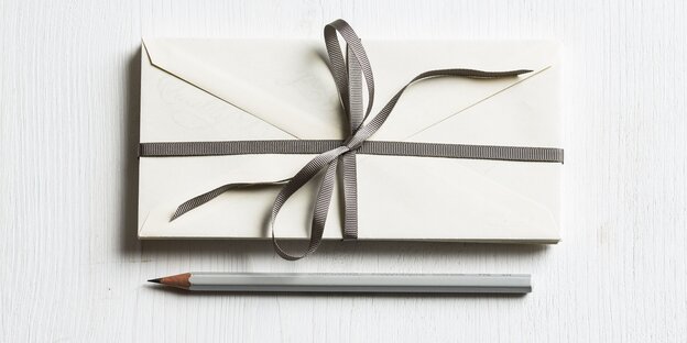 Ein Stapel mit Geschenkband eingewickelter Briefe liegt über einem Bleistift Ein Stapel mit Geschenkband eingewickelter Briefe liegt über einem Bleistift