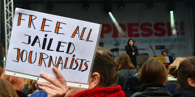 eine Frau hält ein A4-Blatt hoch, darauf steht: „free all jailed journalists“ eine Frau hält ein A4-Blatt hoch, darauf steht: „free all jailed journalists“