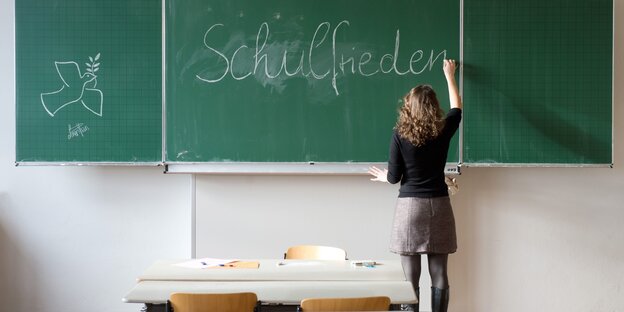 Eine Frau schreibt das Wort "Schulfrieden" auf eine Tafel Eine Frau schreibt das Wort "Schulfrieden" auf eine Tafel