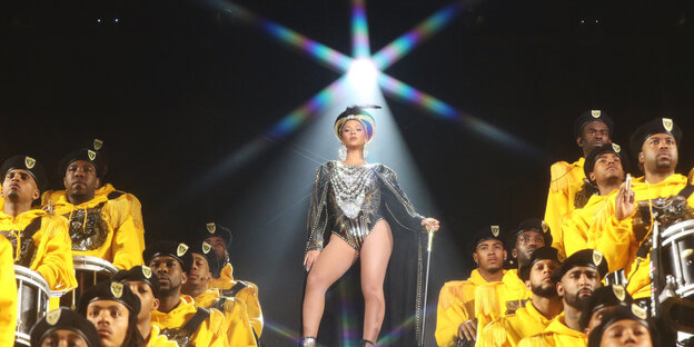 Beyoncé auf der Bühne. Rechts und links Musiker in gelben Pullis. Beyoncé auf der Bühne. Rechts und links Musiker in gelben Pullis.