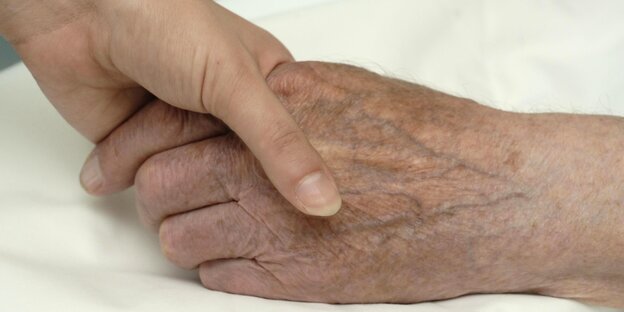 Eine Pflegekraft schiebt in einem Pflegeheim eine Person im Rollstuhl über einen Korridor Eine Pflegekraft schiebt in einem Pflegeheim eine Person im Rollstuhl über einen Korridor