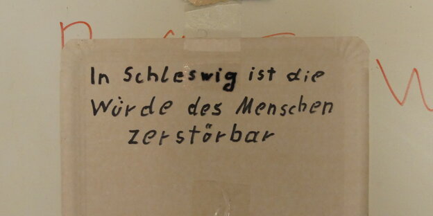 Auf einem Pappteller steht "In Schleswig ist die Würde des Menschen zerstörbar". Auf einem Pappteller steht "In Schleswig ist die Würde des Menschen zerstörbar".