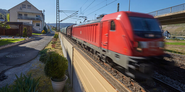 Ein roter Zug fährt an einem Haus vorbei, dazwischen ist eine Lärmschutzwand Ein roter Zug fährt an einem Haus vorbei, dazwischen ist eine Lärmschutzwand