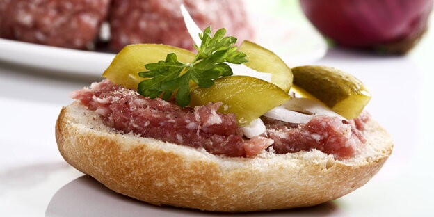 Ein hübsch garniertes Mettbrötchen mit Zwiebeln und Gürkchen