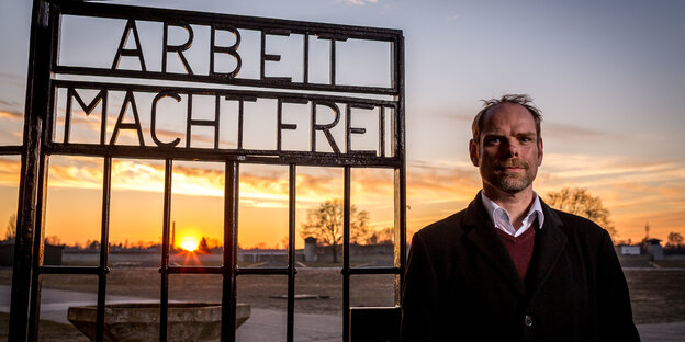 Axel Drecoll steht neben einem Gittertorm it der Inschrift ,Arbeit macht frei' Axel Drecoll steht neben einem Gittertorm it der Inschrift ,Arbeit macht frei'