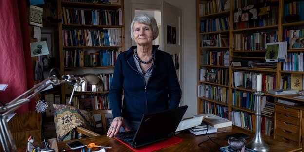 Eine Frau im blauen Kleid steht hinter ihrem Schreibtisch. Der Raum ist voller Bücher Eine Frau im blauen Kleid steht hinter ihrem Schreibtisch. Der Raum ist voller Bücher
