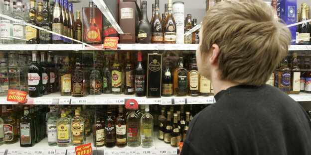 Ein Junge steht in einem Supermarkt vor einem Spirituosenregal Ein Junge steht in einem Supermarkt vor einem Spirituosenregal