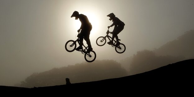 Zwei BMX-Fahrer machen einen Trick auf einer Schanze vor einem Sonnenuntergang Zwei BMX-Fahrer machen einen Trick auf einer Schanze vor einem Sonnenuntergang