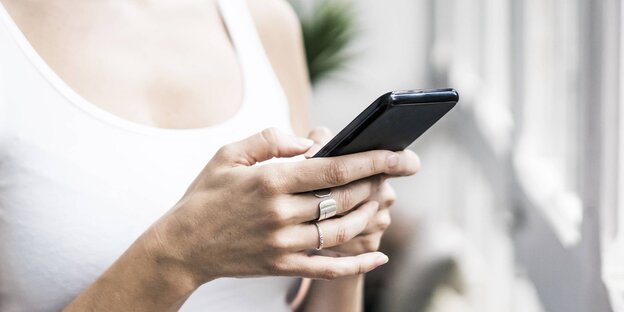 Eine Frau hält ein Smartphone in der Hand und steht vor einem Fenster Eine Frau hält ein Smartphone in der Hand und steht vor einem Fenster