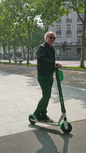 taz-Frankreich-Korrespondent, ein älterer Mann mit weißem Haar, steht auf einem Elektroroller taz-Frankreich-Korrespondent, ein älterer Mann mit weißem Haar, steht auf einem Elektroroller