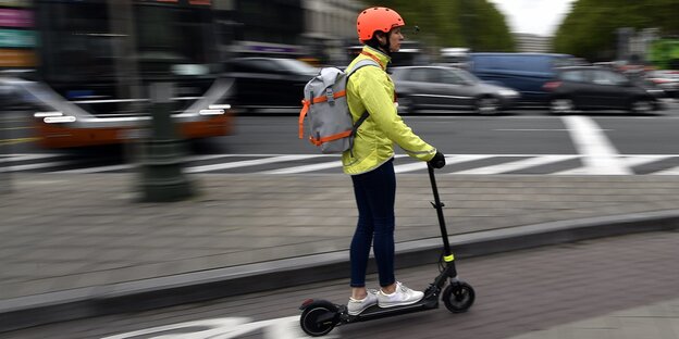 Eine Frau mit Helm fährt mit einem elektronischen Roller auf einem Fahrradweg Eine Frau mit Helm fährt mit einem elektronischen Roller auf einem Fahrradweg
