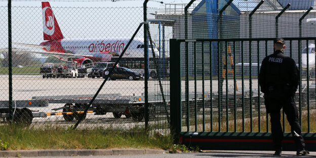 Polizist auf einem Flughafen. Hinter dem Zaun wird ein Flugzeug abgefertigt. Polizist auf einem Flughafen. Hinter dem Zaun wird ein Flugzeug abgefertigt.
