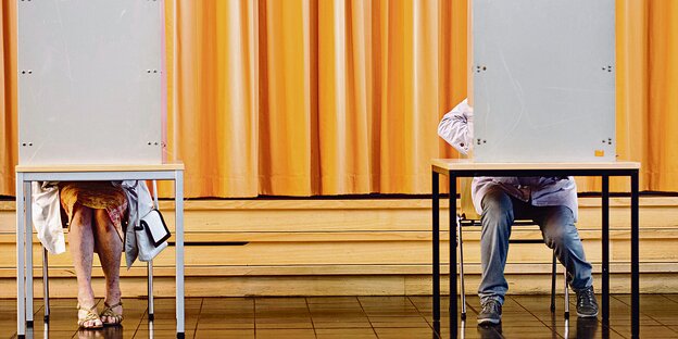 Eine Frau und ein Mann sitzen hinter dem Sichtschutz in einem Wahllokal. Eine Frau und ein Mann sitzen hinter dem Sichtschutz in einem Wahllokal.