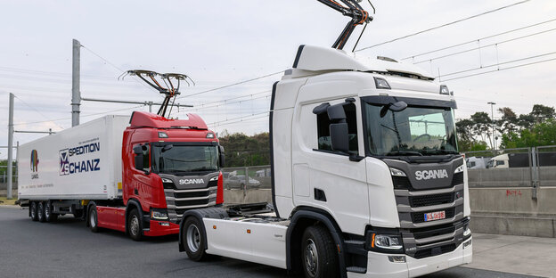 Zwei Lkw stehen auf der Autobahn und docken an der Stromoberleitung an. Zwei Lkw stehen auf der Autobahn und docken an der Stromoberleitung an.