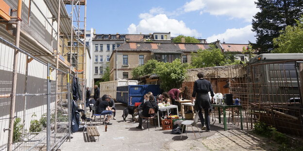 Leute sitzen in einer Einfahrt, im Hintergrund sind sanierte Häuser zu sehen Leute sitzen in einer Einfahrt, im Hintergrund sind sanierte Häuser zu sehen