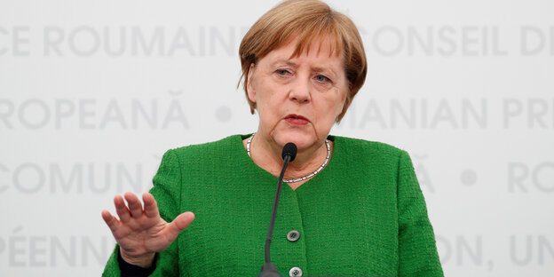 Merkel in grüner Kleidung macht mit der Hand ein abbremsendes Zeichen Merkel in grüner Kleidung macht mit der Hand ein abbremsendes Zeichen