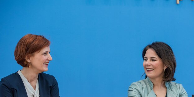 Katja Kipping und Annalena Baerbock strahlen einander an, sie sitzen vor einer blauen Wand Katja Kipping und Annalena Baerbock strahlen einander an, sie sitzen vor einer blauen Wand