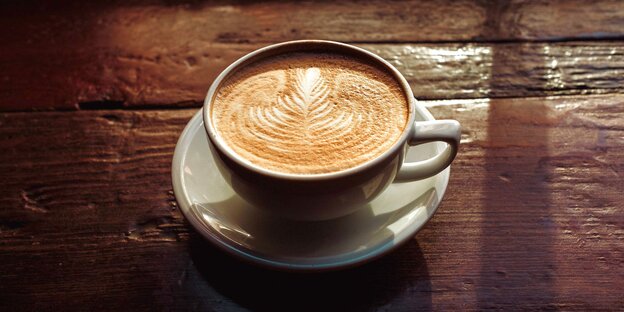 Eine Tasse voller Milchkaffee auf alten Holzdielen stehend Eine Tasse voller Milchkaffee auf alten Holzdielen stehend
